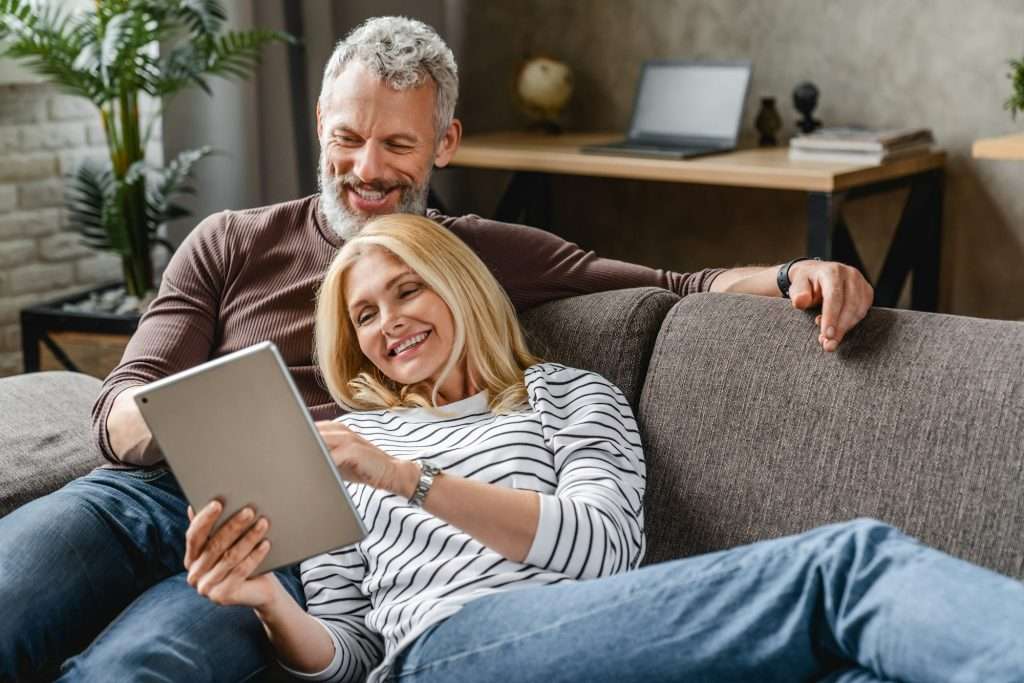 Happy senior couple using digital tablet on sofa indoors