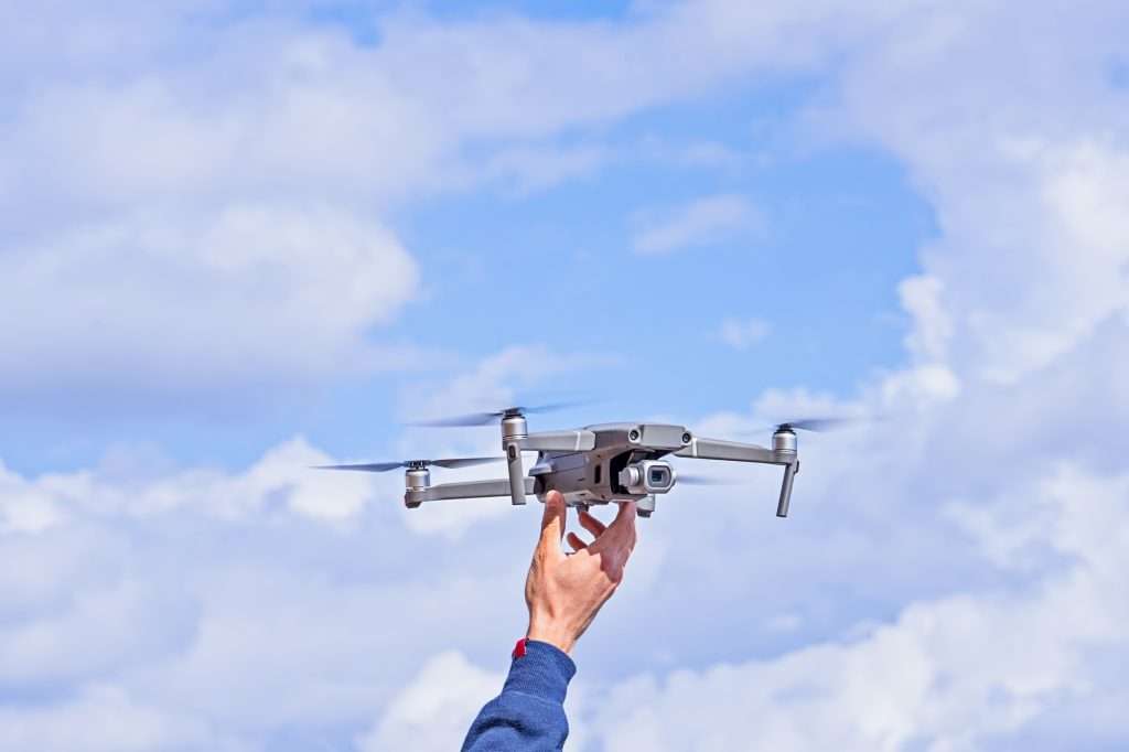 Hand holding a quadcopter drone against cloudy blue sky. Hand Launching Drone